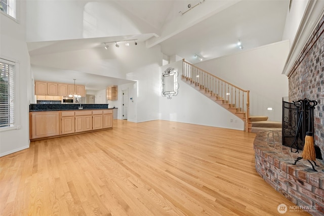 living room featuring a fireplace, high vaulted ceiling, light hardwood / wood-style floors, and sink