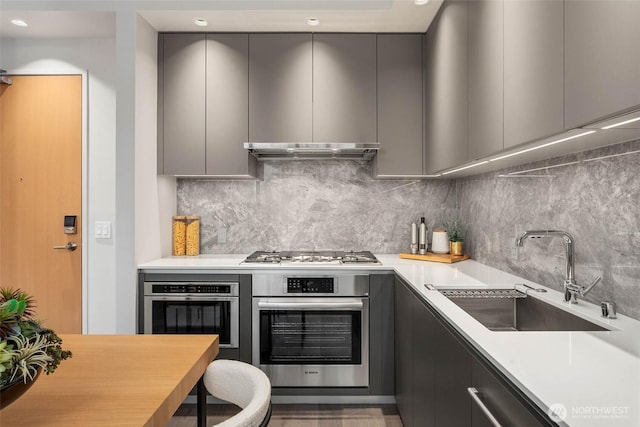 kitchen featuring modern cabinets, appliances with stainless steel finishes, gray cabinetry, under cabinet range hood, and a sink