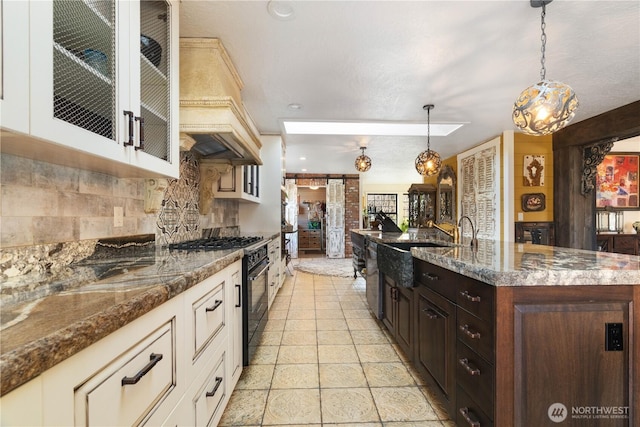 kitchen with custom exhaust hood, hanging light fixtures, glass insert cabinets, dark brown cabinetry, and high end range