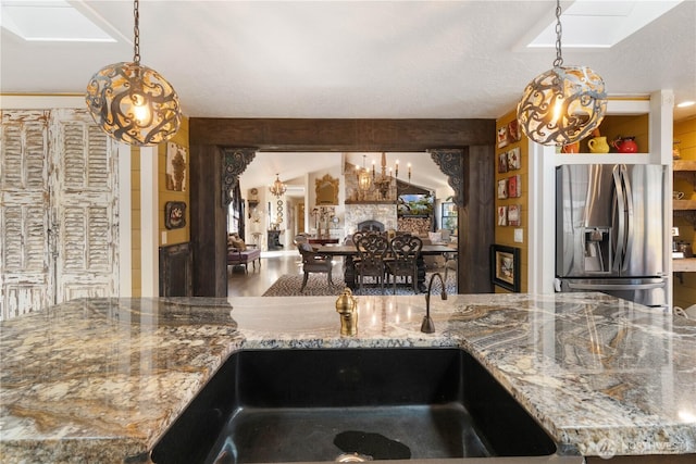 kitchen featuring open floor plan, vaulted ceiling with beams, light stone countertops, stainless steel refrigerator with ice dispenser, and a sink