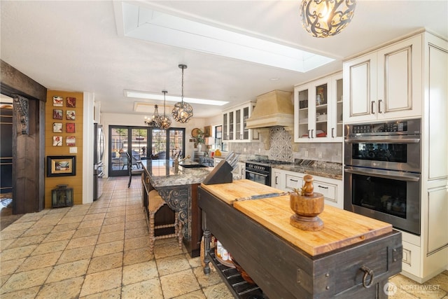 kitchen featuring glass insert cabinets, a center island, hanging light fixtures, custom exhaust hood, and stainless steel appliances