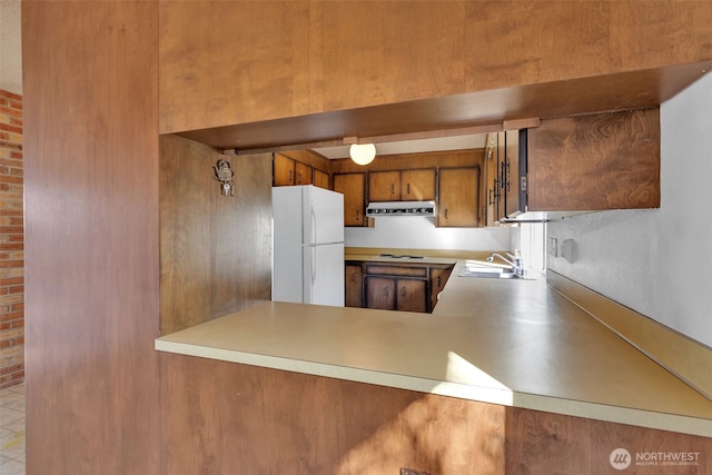 kitchen featuring a sink, ventilation hood, freestanding refrigerator, stovetop, and brown cabinetry