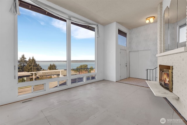 unfurnished living room with concrete floors, a water view, a fireplace, a towering ceiling, and visible vents