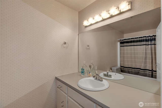 bathroom featuring toilet, wallpapered walls, and vanity