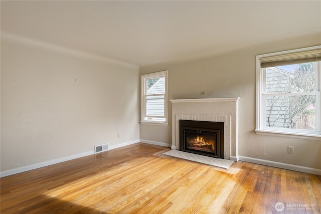 unfurnished living room with a healthy amount of sunlight, visible vents, a fireplace, and wood finished floors