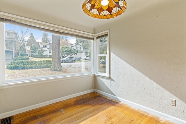 empty room featuring visible vents, a textured wall, baseboards, and wood finished floors