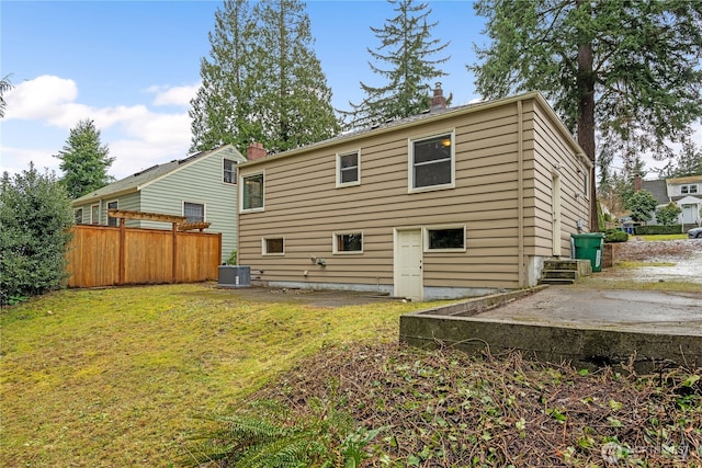 back of property featuring central AC, fence, a lawn, a chimney, and a patio area