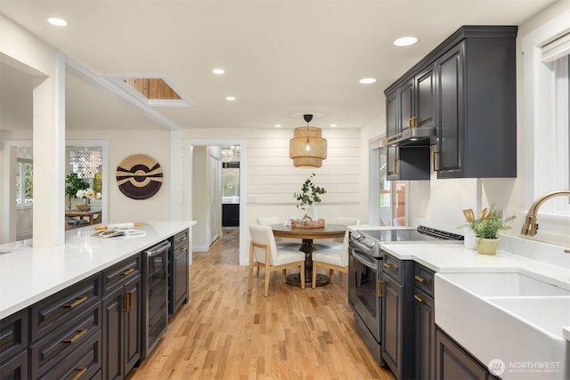 kitchen with electric stove, sink, beverage cooler, light wood-type flooring, and hanging light fixtures