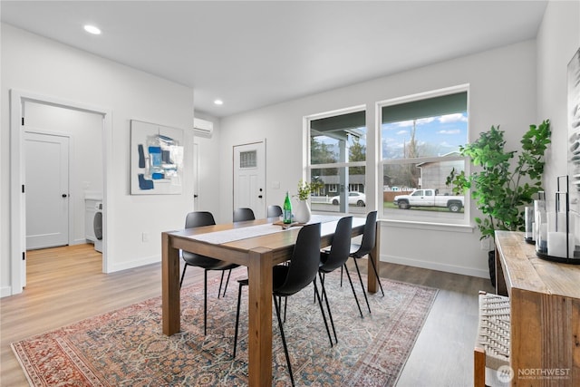 dining room featuring washer / dryer, light wood-style flooring, baseboards, and a wall mounted AC