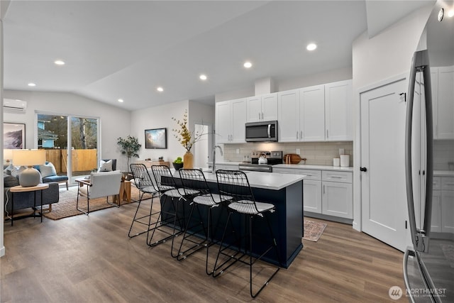 kitchen with a breakfast bar area, wood finished floors, stainless steel appliances, vaulted ceiling, and light countertops