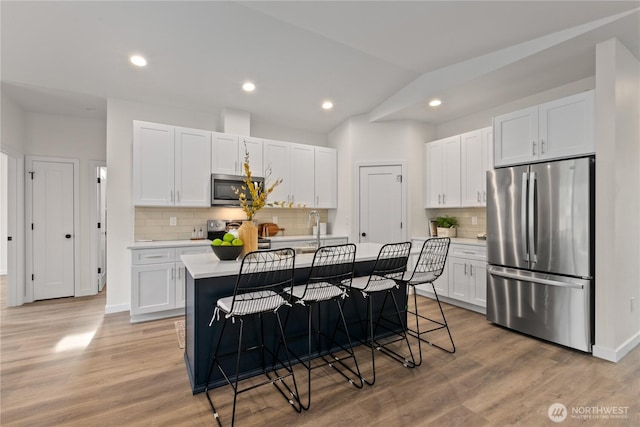 kitchen featuring light countertops, lofted ceiling, appliances with stainless steel finishes, white cabinetry, and a kitchen island with sink