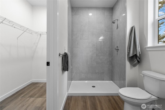 full bath with toilet, wood finished floors, tiled shower, baseboards, and a spacious closet