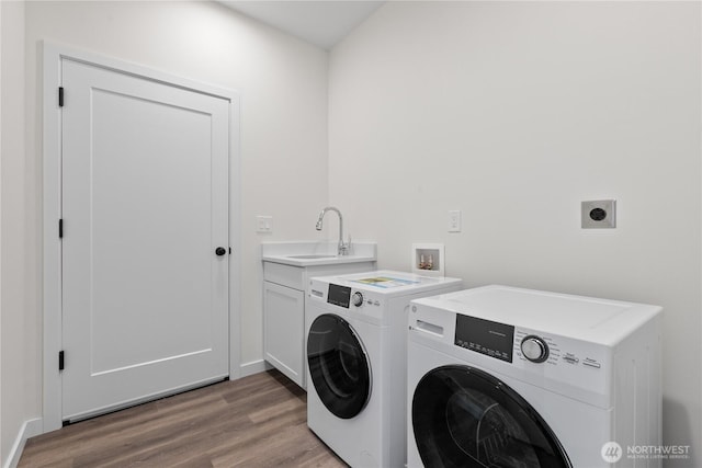 clothes washing area featuring cabinet space, washer and dryer, wood finished floors, and a sink