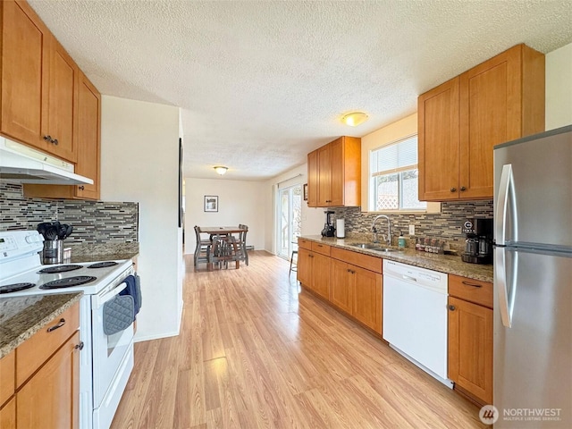 kitchen with white appliances, light stone countertops, decorative backsplash, light hardwood / wood-style floors, and sink