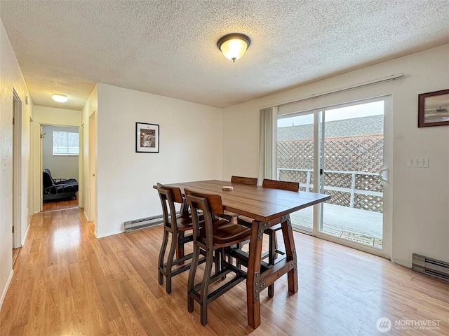 dining space featuring light wood-type flooring, a baseboard radiator, and a textured ceiling