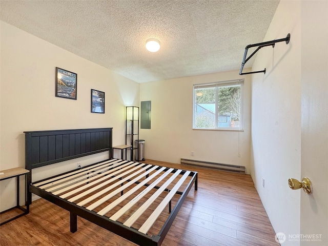 bedroom featuring hardwood / wood-style floors, baseboard heating, electric panel, and a textured ceiling