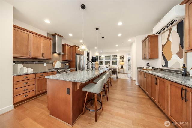 kitchen with a center island with sink, hanging light fixtures, stainless steel appliances, wall chimney range hood, and sink