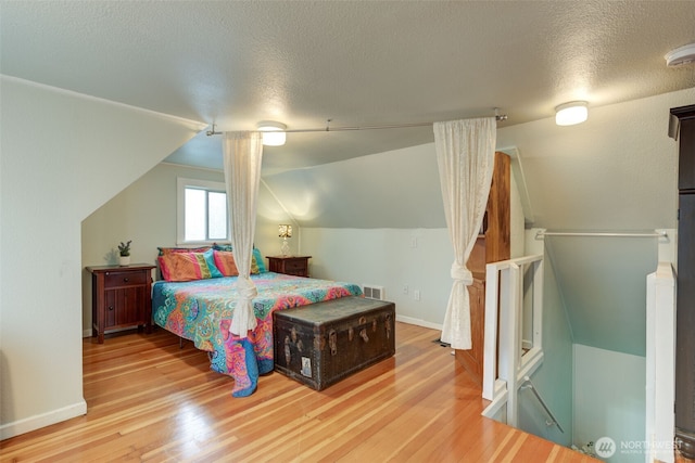 bedroom featuring vaulted ceiling, visible vents, a textured ceiling, and wood finished floors