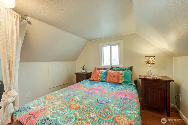 bedroom with lofted ceiling, wood finished floors, baseboards, and a textured ceiling