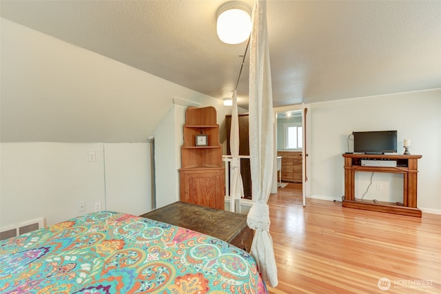 bedroom featuring visible vents, a textured ceiling, wood finished floors, baseboards, and lofted ceiling