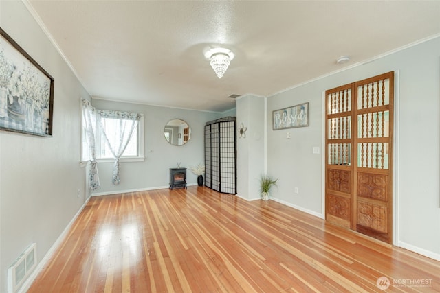 interior space featuring visible vents, light wood-style flooring, crown molding, baseboards, and a wood stove