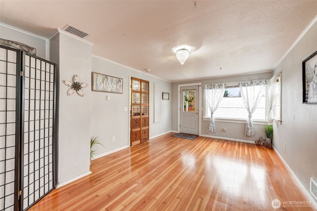 foyer entrance with hardwood / wood-style floors, baseboards, visible vents, a textured ceiling, and crown molding