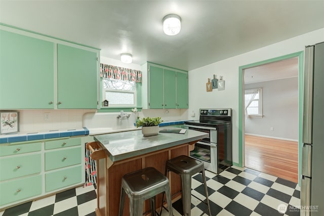 kitchen with a kitchen island, light countertops, appliances with stainless steel finishes, tile patterned floors, and a kitchen breakfast bar