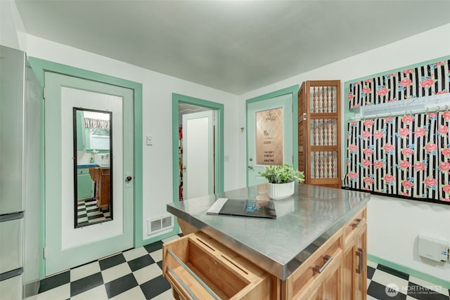 kitchen with visible vents, light floors, stainless steel counters, and a kitchen island