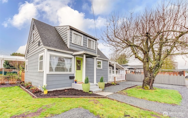 view of front of property with roof with shingles, a front lawn, and fence