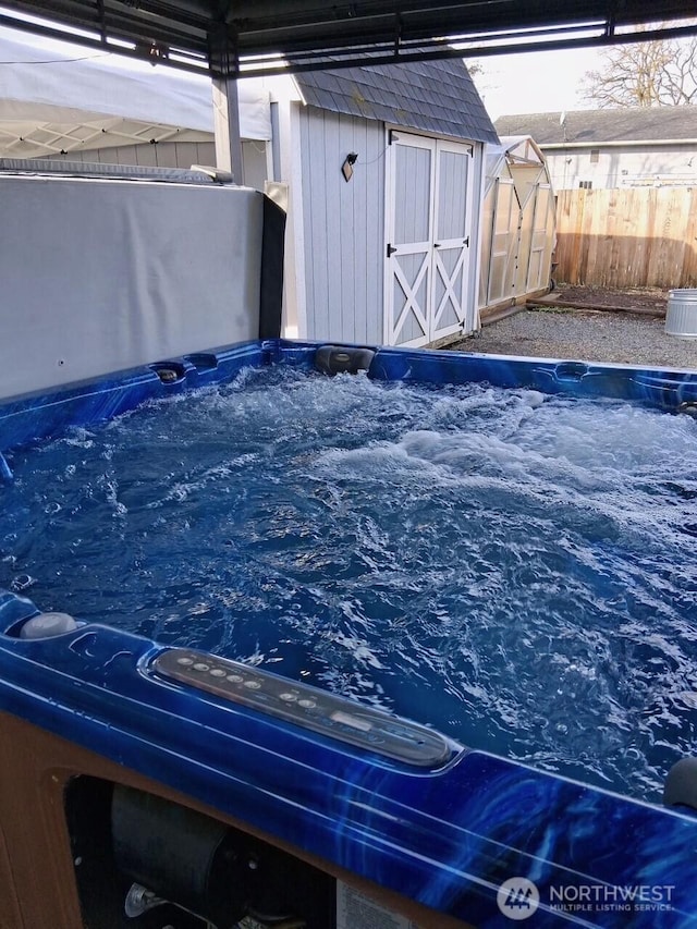 view of swimming pool with a hot tub, a storage shed, an outdoor structure, and fence