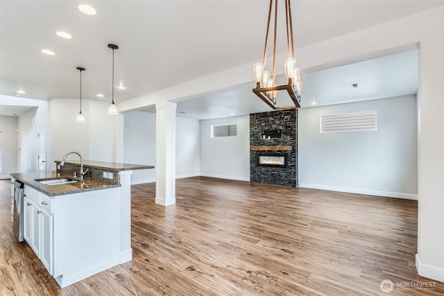 kitchen featuring visible vents, a large fireplace, dark stone counters, wood finished floors, and a sink