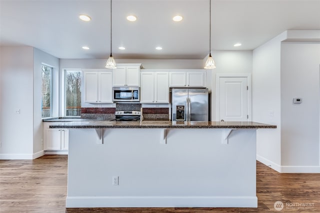 kitchen with appliances with stainless steel finishes, white cabinetry, a kitchen breakfast bar, and wood finished floors