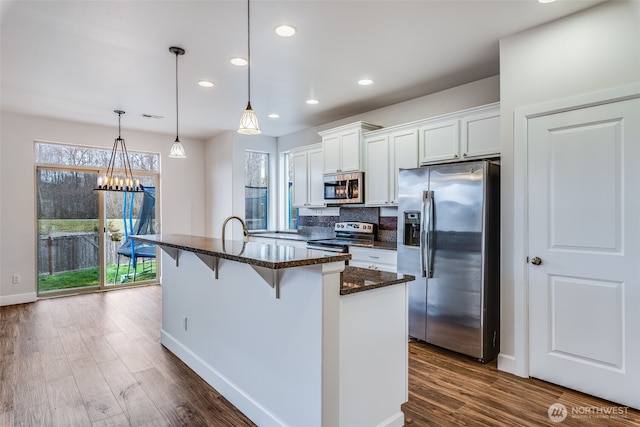 kitchen featuring a breakfast bar area, dark wood-type flooring, appliances with stainless steel finishes, white cabinetry, and backsplash