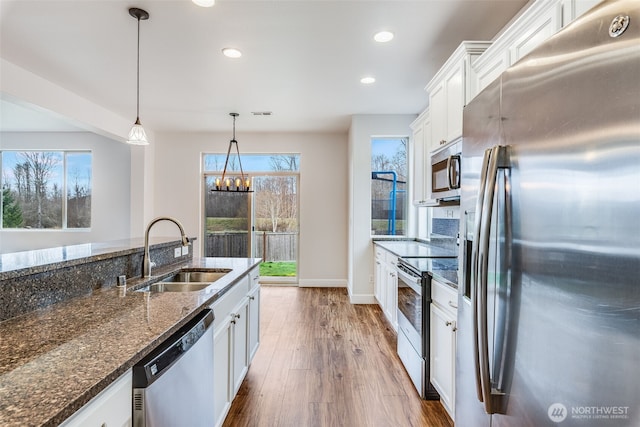 kitchen with pendant lighting, appliances with stainless steel finishes, wood finished floors, white cabinetry, and a sink