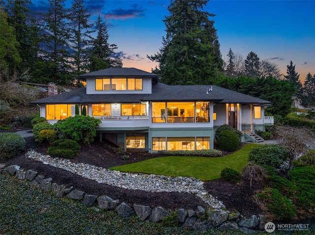 back of property at dusk with a sunroom, a lawn, and a chimney