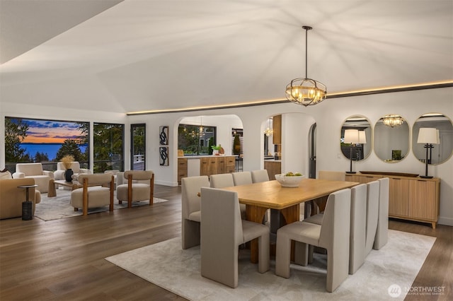 dining space with arched walkways, radiator, an inviting chandelier, vaulted ceiling, and wood finished floors