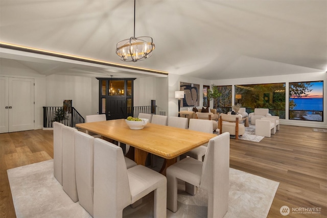 dining space featuring light wood-type flooring, vaulted ceiling, and an inviting chandelier