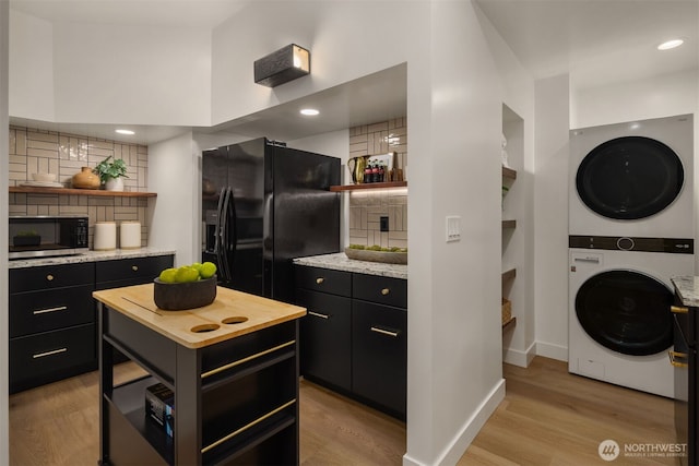 kitchen with stacked washing maching and dryer, stainless steel microwave, open shelves, and black fridge