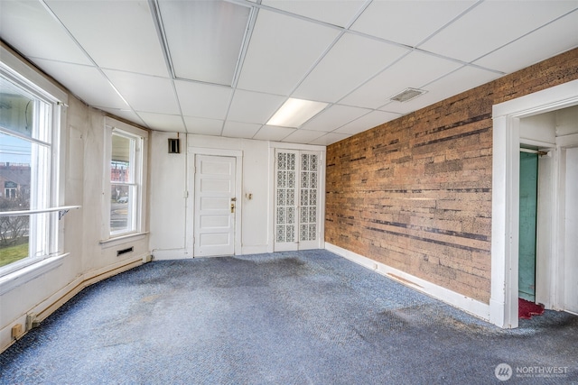 spare room featuring a drop ceiling, wood walls, visible vents, baseboard heating, and carpet