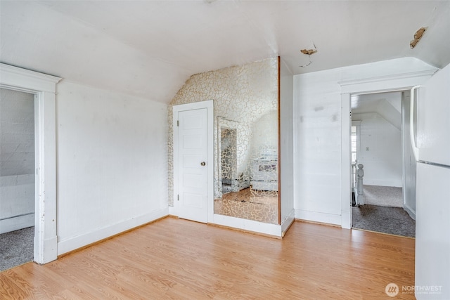 unfurnished bedroom featuring lofted ceiling, freestanding refrigerator, baseboards, and wood finished floors