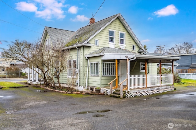 view of front of property with a porch, roof with shingles, and a chimney