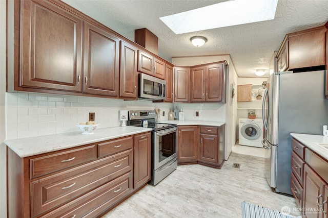 kitchen featuring stainless steel appliances, a skylight, light countertops, and washer / dryer