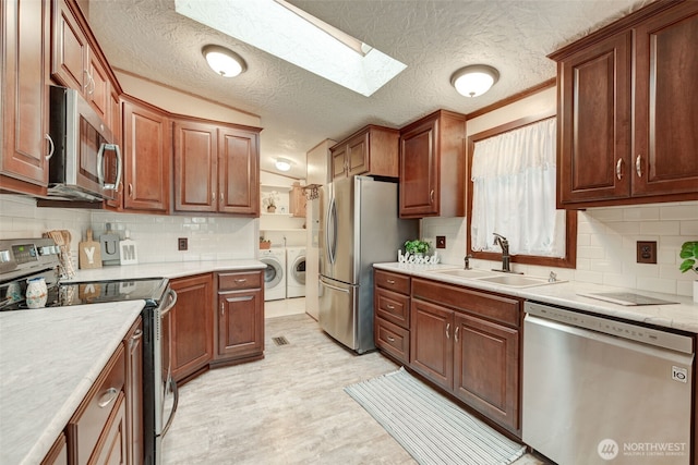 kitchen featuring a skylight, tasteful backsplash, appliances with stainless steel finishes, independent washer and dryer, and a sink