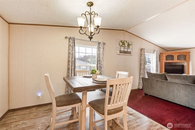 dining area with a healthy amount of sunlight, a chandelier, wood finished floors, and lofted ceiling