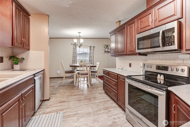 kitchen with a notable chandelier, stainless steel appliances, light countertops, light wood finished floors, and pendant lighting