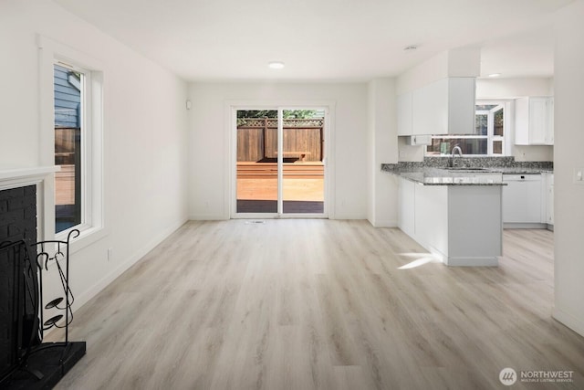 unfurnished living room with baseboards, a sink, and light wood finished floors