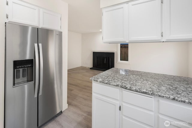 kitchen featuring light stone counters, light wood-type flooring, white cabinets, and stainless steel refrigerator with ice dispenser