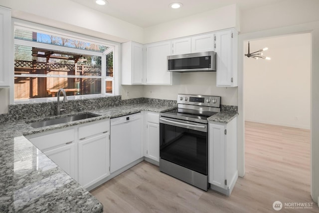 kitchen with light stone counters, a sink, white cabinets, light wood-style floors, and appliances with stainless steel finishes