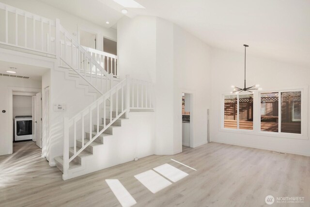 interior space with high vaulted ceiling, washer / clothes dryer, wood finished floors, and a notable chandelier