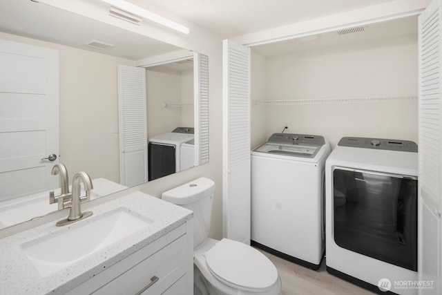 bathroom with toilet, washing machine and dryer, visible vents, and vanity